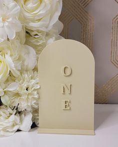 there is a small white tombstone with the word one on it next to some flowers