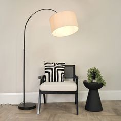 a black and white chair sitting under a floor lamp next to a potted plant