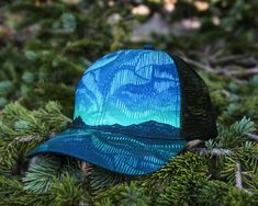 Have you seen them? Dazzling ribbons of light dance in the night sky on our Northern Lights Trucker Hat. Whether you've seen them in person or dream of glimpsing the aurora borealis, our hat is the perfect fit. The artwork was hand-carved and printed with traditional block printing tools and digitally colored. ITEM DETAILS Alpinecho's trucker hats are made in partnership with Purnaa, a social enterprise and World Fair Trade Organization Guaranteed Member (WFTO) in Nepal with a mission to create Artistic Adjustable Hats As Gift, Unique Adjustable Cap, Blue Handmade Outdoor Hat, Artistic Adjustable Blue Hat, Handmade Blue Outdoor Hat, Unique Blue Adjustable Hat, Unique Adjustable Blue Hat, World Fair, Social Enterprise