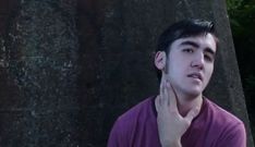 a young man standing in front of a tree with his hand on his face as if to hear something