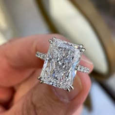 a person holding an engagement ring with a princess cut diamond in it's center