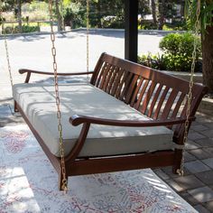 a wooden swing bed sitting on top of a white and red rug next to a tree