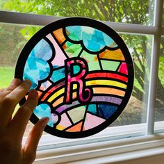 a hand is holding up a stained glass window with the letter b in it's center