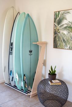 three surfboards are leaning against the wall in a room with tile flooring and potted plants