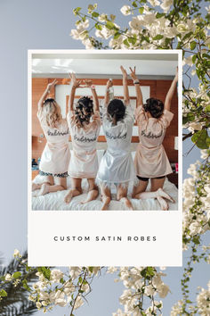 four women in white robes are sitting on a bed with their arms up and the words custom satin robes above them