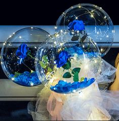 two clear vases with blue flowers and lights in them sitting on a window sill