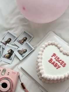 a white cake with pink frosting and pictures on it, next to a camera