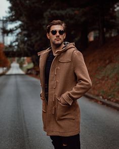 a man standing in the middle of an empty road wearing sunglasses and a coat over his shoulders