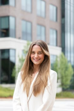 a woman with long hair standing in front of a tall building smiling at the camera