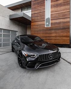 a black car parked in front of a house with wood siding on the side of it