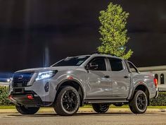 a silver pick up truck parked in front of a house at night with its lights on