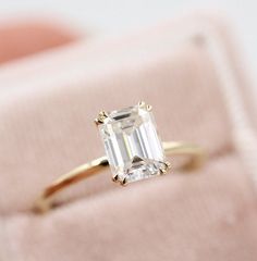 an emerald - cut diamond ring sits on a pink velvet box