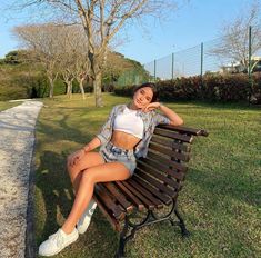 a woman sitting on top of a wooden bench in the grass next to a park