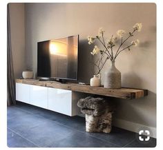 a flat screen tv sitting on top of a wooden shelf next to a vase with flowers