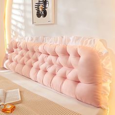 a pink couch sitting on top of a bed next to an open book and vase