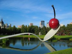 a woman with glasses and a cherry on top of a sculpture in front of a lake