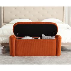 an orange storage ottoman with pillows and blankets on it in front of a white bed