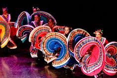 several women in colorful costumes are dancing with large fan shaped skirts on their heads and legs