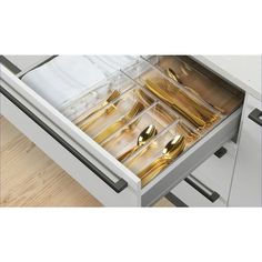 an open drawer with gold utensils in it on a wooden floor next to white cabinets