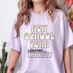 Our "Back To School Shirt" is a fun blend of retro aesthetics and humorous anticipation for the upcoming academic year. With its vintage distressed graphic, this retro shirt proudly displays the phrase "New School Year" in bold, eye-catching lettering. Adding a playful twist to the design, the shirt also features the phrase "Loading..." below, capturing the excitement and anticipation that comes with the first day of school. Perfect for teachers and students alike, this funny T-shirt is a must-h Cotton T-shirt For College Events, End Of School Year, Trendy College Shirt With Graphic Print, Trendy Graphic Print Shirt For College, Screen Print Tops For College, School Spirit Shirt With Letter Print For College Events, Back To School Spirit Shirt With Text Print, School Spirit Shirt With Graphic Print For College Events, Retro Graphic Print Shirt For School, Graphic Print Shirt For College Events