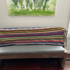 a wooden bench with a colorful blanket on it's back and a painting hanging above the bench