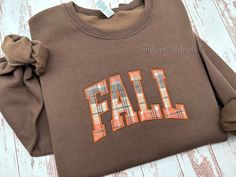 Fall Plaid Applique Embroidered Sweatshirt A perfect sweatshirt to wear throughout the Autumn season! The sweatshirt is appliqued with a cute fall plaid fabric giving it a fun festive look. *Listing photo sweatshirt color is Chocolate Brown. Enjoy a classic soft sweatshirt that's custom embroidered for you. The shirt is medium-weight, making it perfect for cool fall evenings and crisp winter days. You can't go wrong with a new favorite sweatshirt to complement a comfy pair of jeans. Each shirt i Varsity T-shirt With Embroidered Graphics For Fall, Long Sleeve T-shirt With Embroidered Graphics For Fall, Brown Sweatshirt For College In Fall, Fall School Spirit T-shirt With Letter Embroidery, School Spirit T-shirt With Letter Embroidery For Fall, Fall School Spirit Embroidered Sweatshirt, Fall College Sweatshirt With Embroidered Text, College Fall Sweatshirt With Embroidered Text, Embroidered Fall College T-shirt