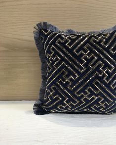 a black and gold decorative pillow on a white bed with wood wall in the background