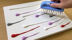 a person is using a brush to paint different colored toothbrushes on a white board