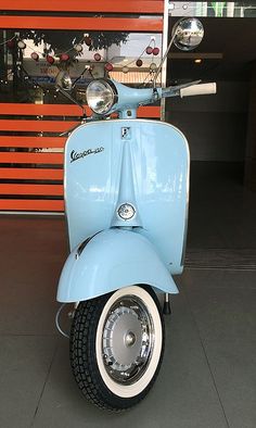 a light blue scooter parked in front of a red building with an orange wall