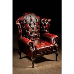 a red leather chair sitting on top of a cement floor next to a black wall