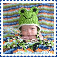 a baby wearing a frog hat laying on top of a blanket