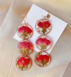 four red flowers are in glass earrings on a white sheet with a card next to it