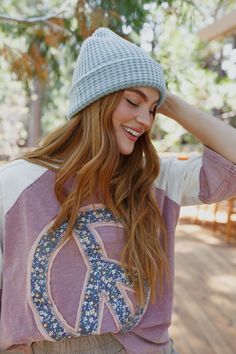 a woman with long hair wearing a purple shirt and a gray knitted beanie