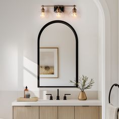 a bathroom with an arched mirror and wooden cabinetry, along with a gold vase filled with flowers