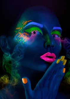 a woman's face with bright makeup and neon colors on her body, holding her hands to her chin