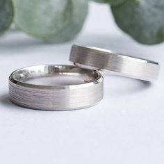 two wedding rings sitting next to each other on top of a white table with succulents in the background