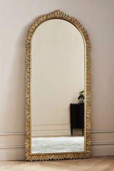 a large gold mirror sitting on top of a hard wood floor next to a plant