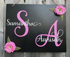 a black sign with pink flowers hanging from it's side on a wooden fence