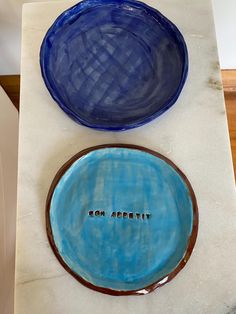 two blue plates sitting on top of a white counter next to each other with words written on them