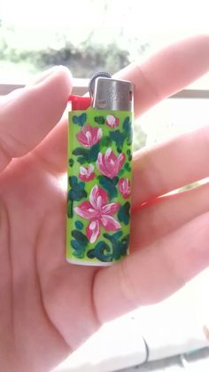 a hand holding a lighter with flowers painted on it's front end and bottom part