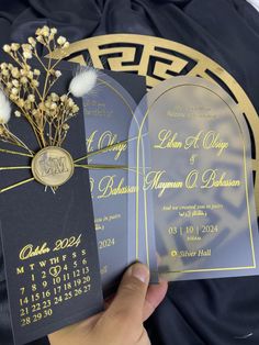 a person holding two black and gold wedding cards