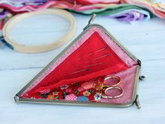 a triangle shaped case with scissors inside on a white wooden table next to colorful fabrics