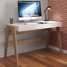 a desktop computer sitting on top of a white desk next to a brick wall and wooden floor