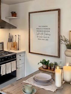 a kitchen table with plates and candles in front of a framed quote on the wall