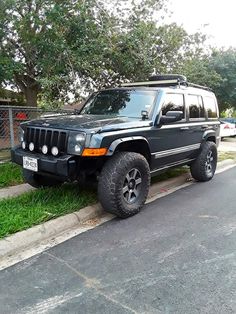 a black jeep parked on the side of a road next to a tree and fence