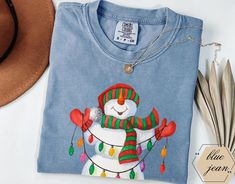 The Retro Snowman Shirt from Comfort Colors is a charming addition to any holiday wardrobe, featuring a delightful snowman adorned with festive Christmas lights. This cute and minimalist tee is designed specifically for women, making it a perfect choice for holiday gatherings or casual outings. Crafted for comfort, it serves as an ideal Christmas gift, combining style and seasonal cheer effortlessly. Custom & Unique tshirts are manufactured with premium quality materials, fits true to size and f Retro Snowman, Cute Christmas Shirt, Xmas Shirts, Holiday Wardrobe, Shirt For Women, Holiday Gathering