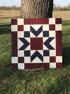 a red, white and blue patchwork quilt sitting next to a tree in the grass