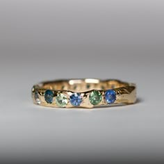 a yellow gold band with blue and green stones on the inside, set against a gray background