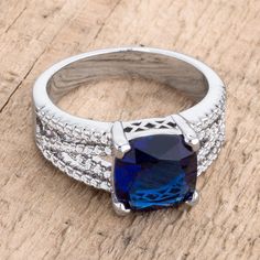 a ring with a blue stone surrounded by white diamonds on a wooden surface in close up view