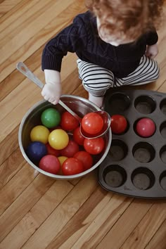 a toddler is playing with colored eggs in a muffin pan on the floor